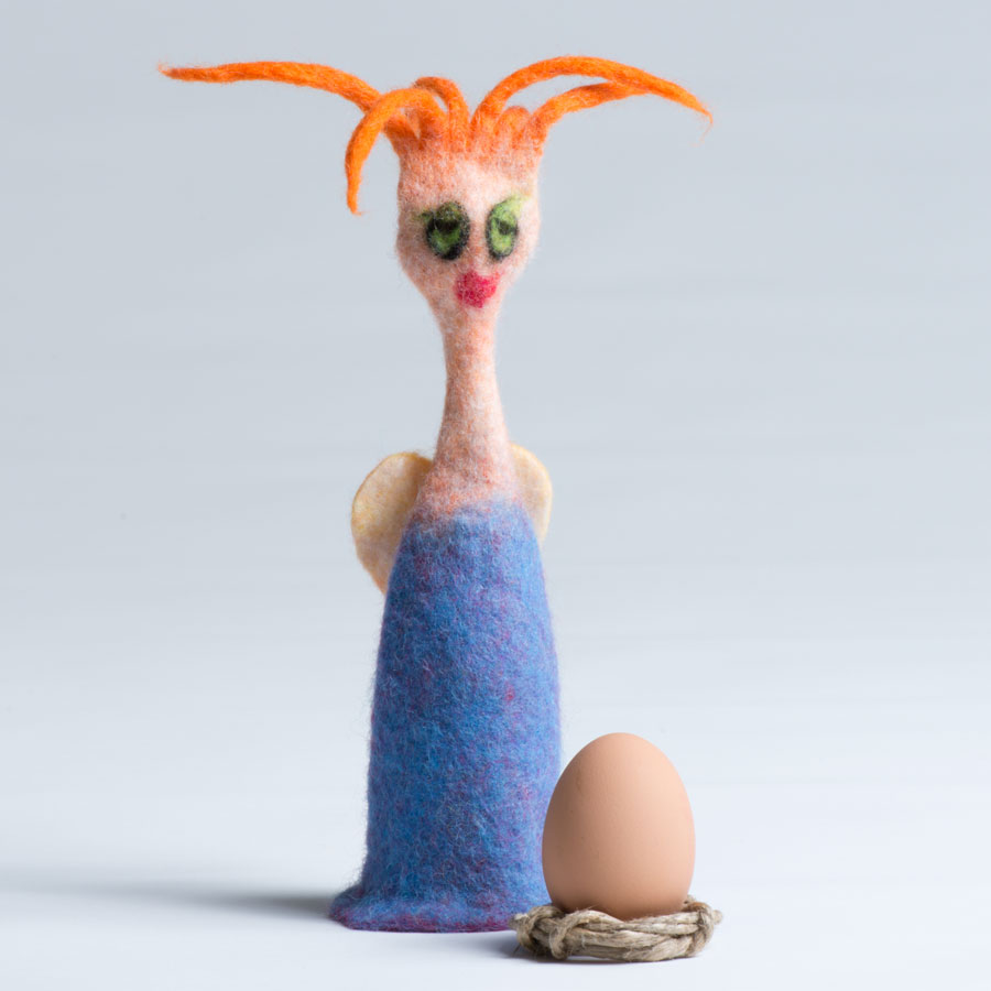 Das Bild zeigt einen "Hausgeist" mit Engelsflügeln, orangenem Haar und blauem Kleid, der auch ein Ei wärmen kann. Vor ihm steht ein Hühnerei.